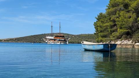 Small boat floating on calm water with a larger vessel in the background.