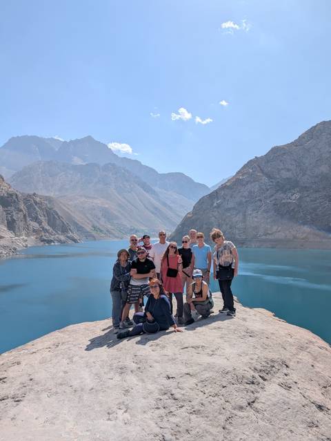 Group of tourists posing by a lake with mountains in the background.