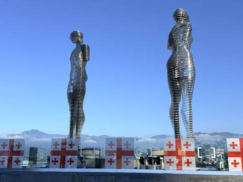       Statues of a man and woman facing each other with a mountainous backdrop.
  