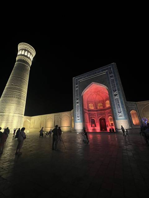 People walking in front of a beautifully lit mosque at night.
