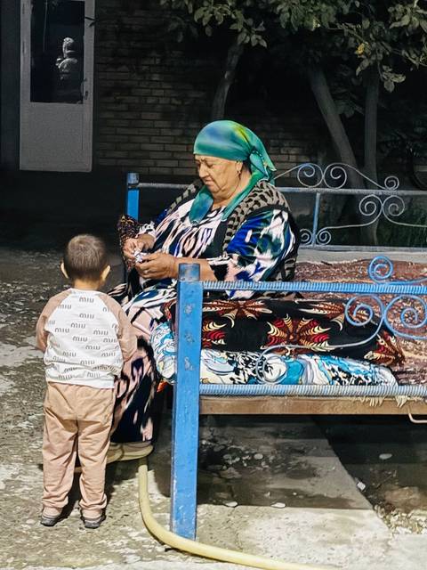       Grandparent with grandchild outdoors on a bed like structure.
  