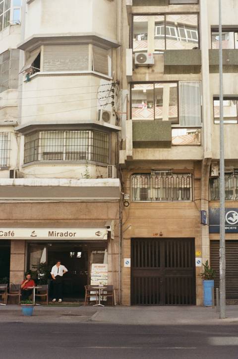      Street view of residential buildings with a café entrance.
  