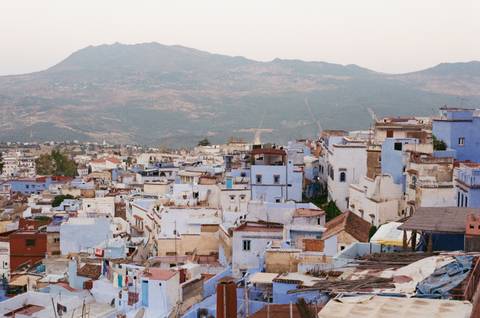       Panoramic view of a city with blue buildings surrounded by mountains.
  
