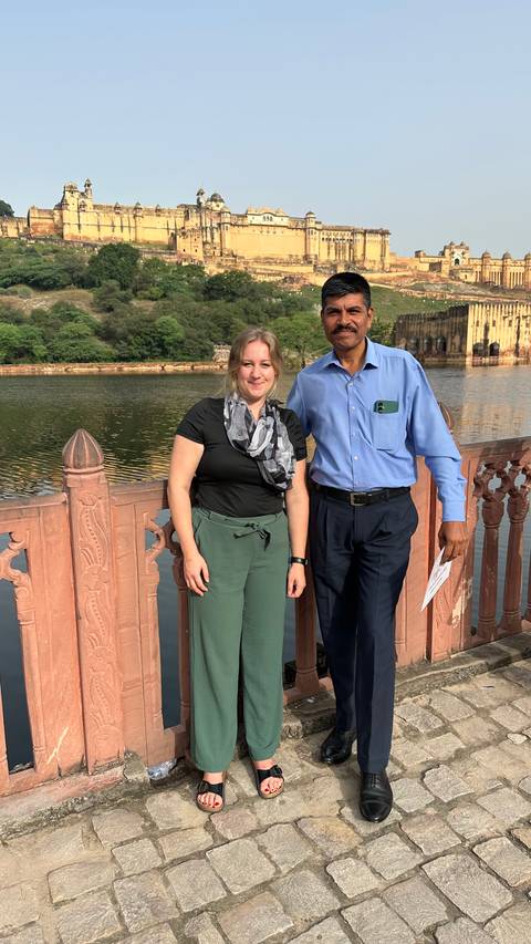 Two people posing by a railing with water in the background.