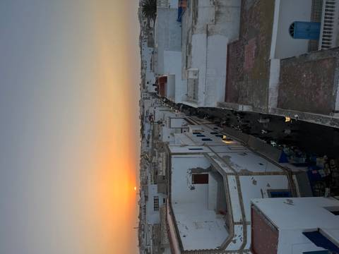       Cityscape at sunset with white buildings and a clear view of the horizon.
  