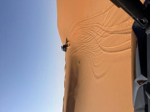       A vehicle ascending a sand dune in a desert landscape.
  