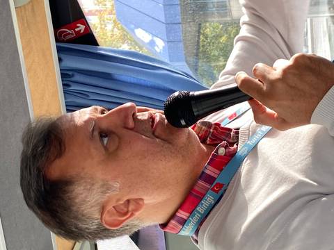 A man speaking into a microphone on a tour bus.
