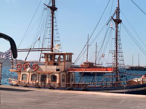       Wooden boats docked at a seaside harbor with a Greek flag.
  