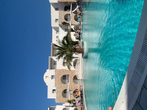       Resort with a swimming pool and palm tree in the center, white buildings around.
  