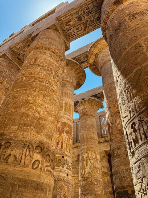 Colossal stone columns with intricate hieroglyphs under blue sky.