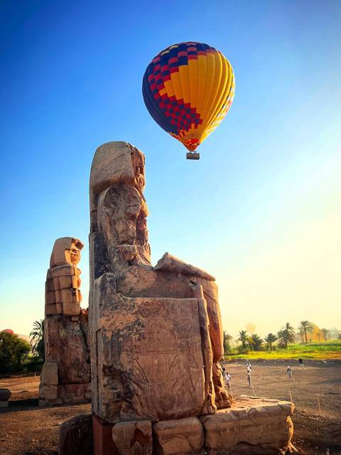 Hot air balloon floating over ancient stone statue.