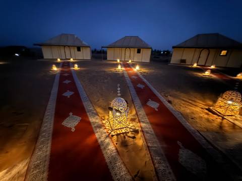       Illuminated tents set up in a desert with lanterns and carpets.
  