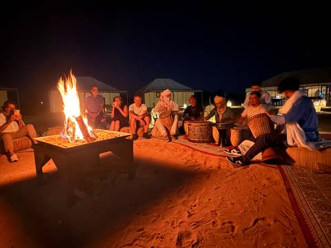       Group of people seated around a campfire in a desert camp setting.
  