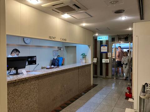Hotel reception area with a staff member at the front desk and guests.