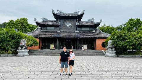       Couple standing in front of a traditional temple building with ornate roof.
  