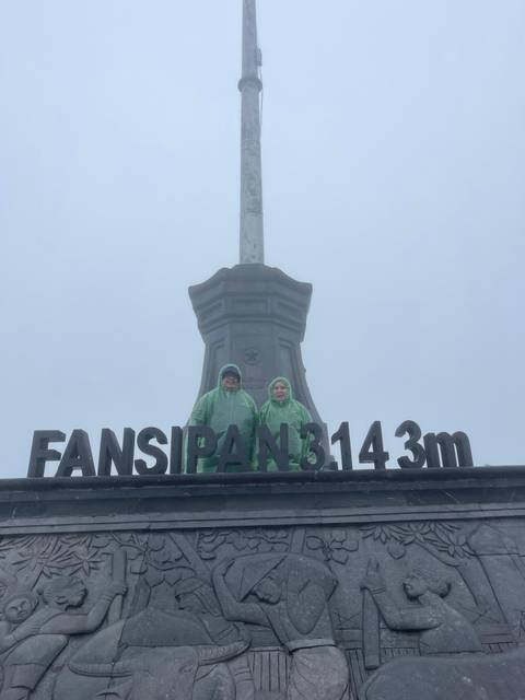       Two people in rain gear at a mountain peak with a sign.
  