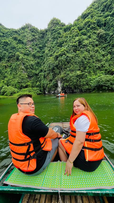       People in life jackets on a boat with green landscape around.
  