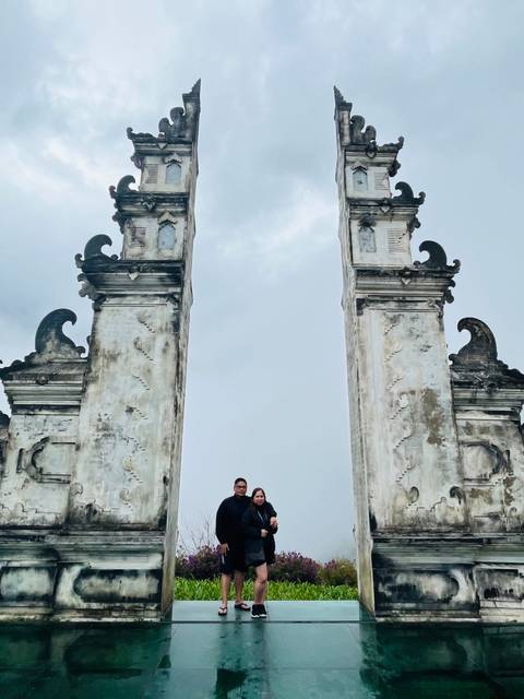       People standing between two tall stone pillars against a cloudy sky.
  