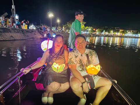       Couple on a boat at night with decorative lanterns and river.
  