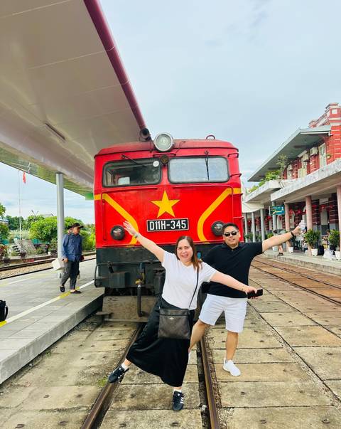       Two people posing in front of a red train at a station.
  
