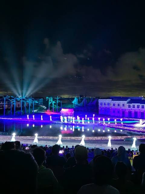       Nighttime show with colorful lights and illuminated figures near water.
  
