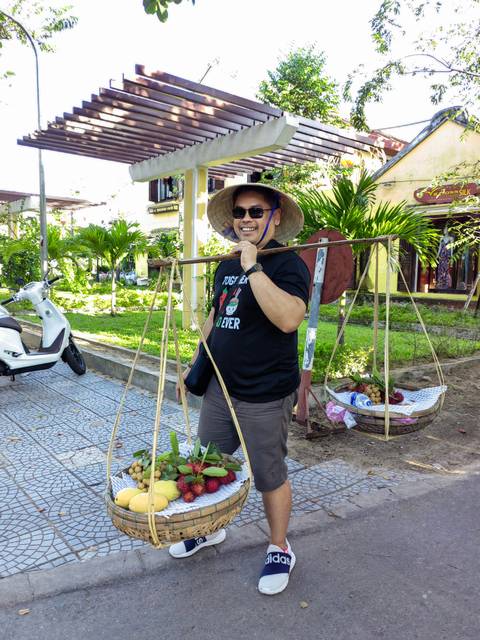       Man smiling while balancing a traditional fruit basket.
  