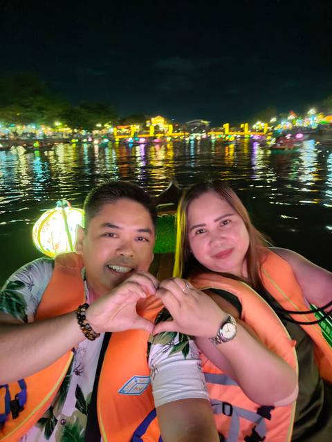       Couple sitting in a boat with colorful lights reflecting on the water.
  