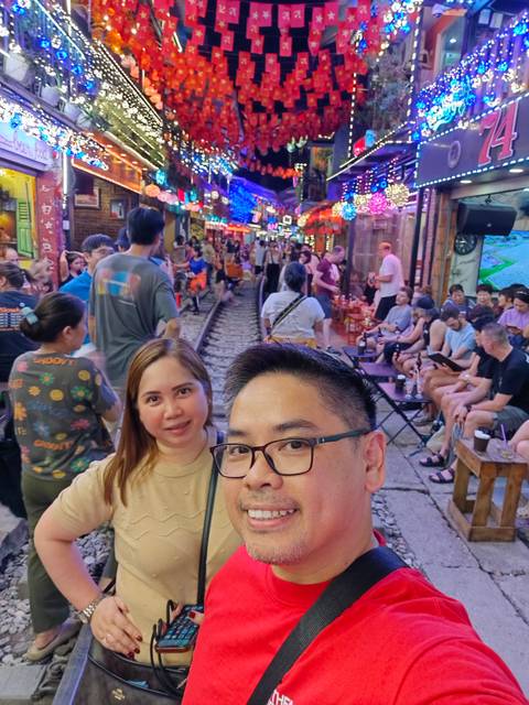       People sitting and socializing along a narrow railway track with buildings in the background.
  