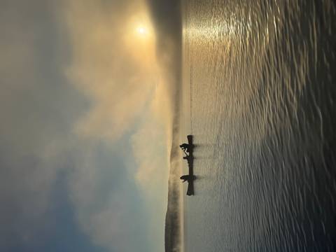       Canoe on a lake with mist and sunrise in the background.
  