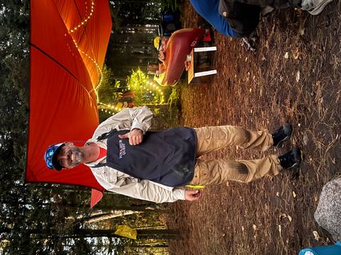       Person standing near a tent camp setup in the woods.
  