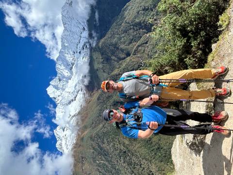 Two people posing with hiking poles in front of snow-capped mountains.