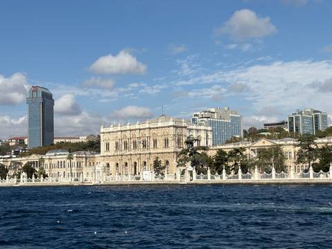       Elegant riverside palace seen from the water with a backdrop of modern buildings.
  