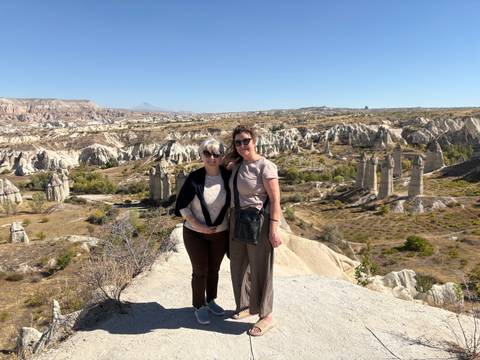       Two people standing together in a rocky landscape with unique geological formations under a clear sky.
  