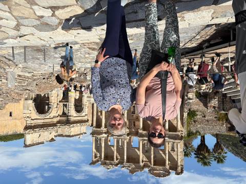       Two people standing in front of ancient ruins with a clear blue sky.
  