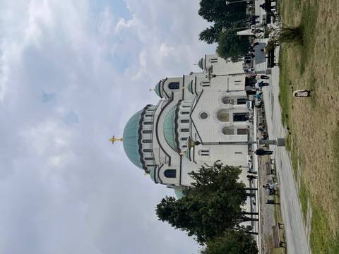       Large domed cathedral with people walking in a square under cloudy skies.
  