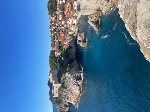       Coastal cityscape with fortifications and red-roofed buildings along a clear blue sea.
  