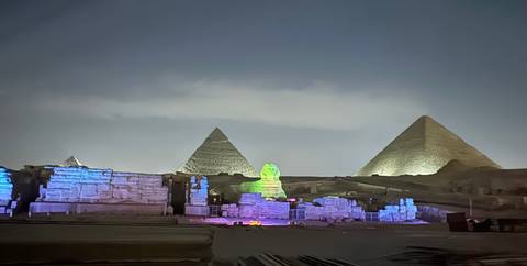 A nighttime view of the pyramids and the Sphinx illuminated with colorful lights.