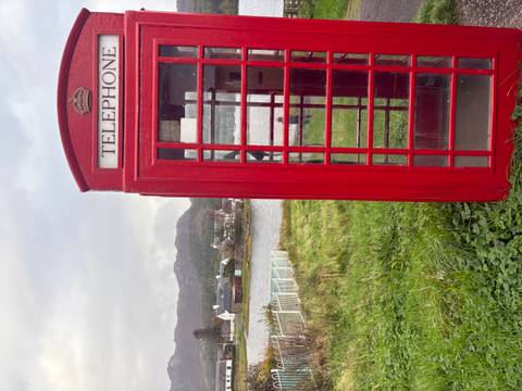       A red telephone booth near a lake and small village.
  