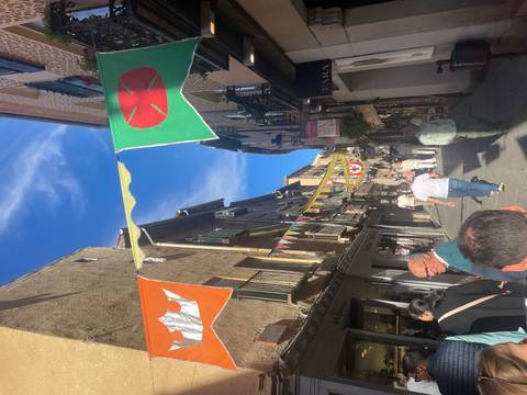 People walking in a lively historic street with flags.