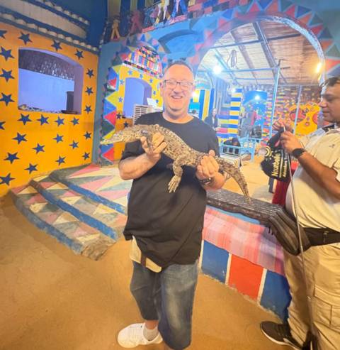 Person holding a small crocodile in a colorful room.