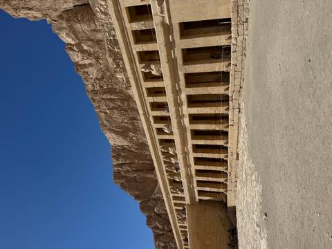 Facade of an ancient temple with statues in a desert landscape.