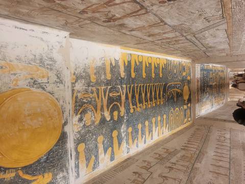 People inside an ancient Egyptian tomb with painted ceiling.