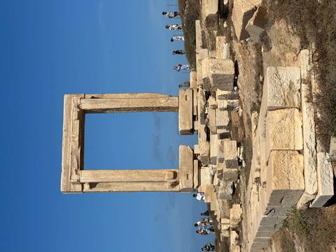 Ancient Portara Gate ruins in Naxos with people exploring.