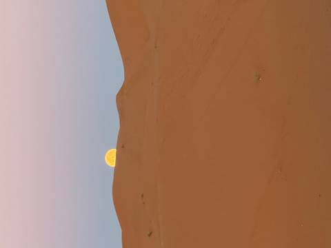 Full moon rising over sand dunes in a desert landscape.