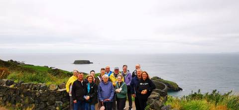       A group of people posing on a coastal path with the ocean in the background.
  