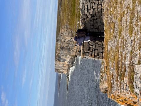       A person photographing a coastline with rocky cliffs and ocean views.
  