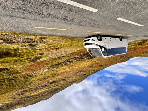       A white tour bus parked on a scenic road with rolling hills.
  