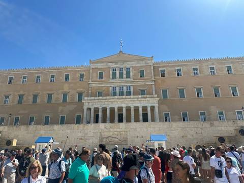       Front view of a neoclassical building with people gathered
  