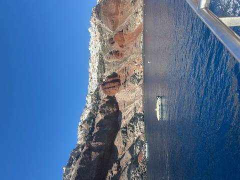       Sailboat on blue water with rocky cliff in Santorini
  