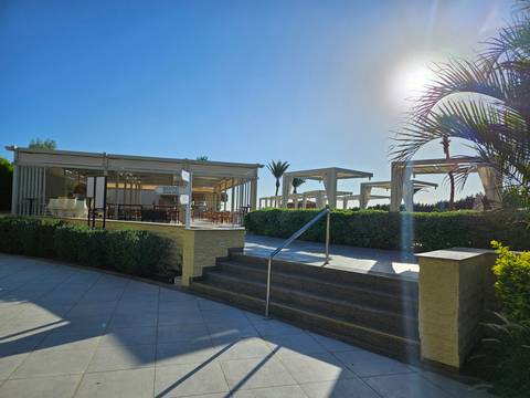       Outdoor cafe area with tables and chairs under a clear blue sky.
  